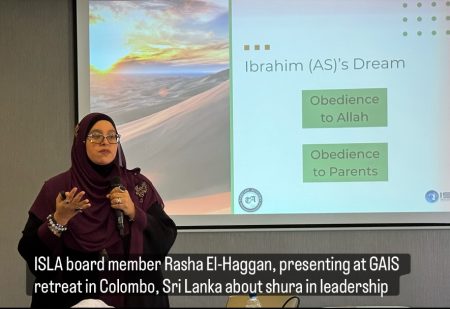 Rasha holding a mic presenting in Sri Lanka with her presentation behind her